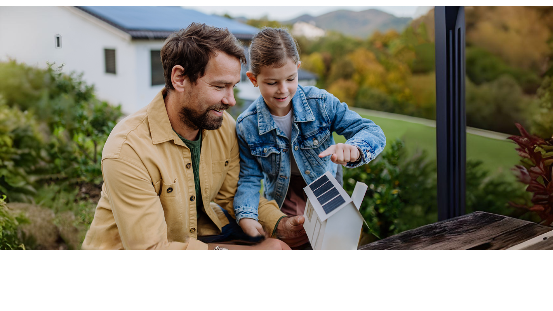 Vader en dochter kijken samen naar een modelhuis met zonnepanelen.
