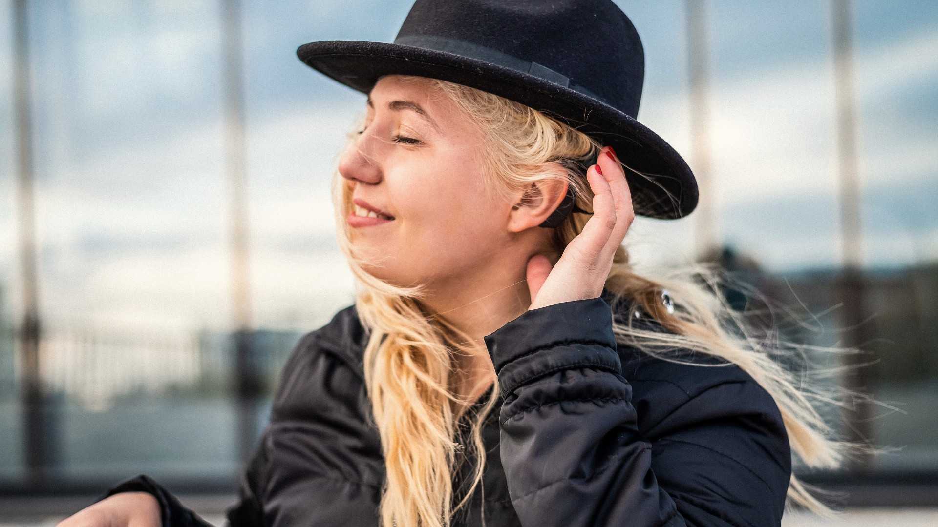 Een lachende vrouw met een zwarte hoed raakt het hoortoestel achter haar oor aan